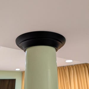 May include: A light green cylindrical column with a black decorative top. The column is smooth and appears to be made of a solid material. The top is a rounded, flat disc shape.