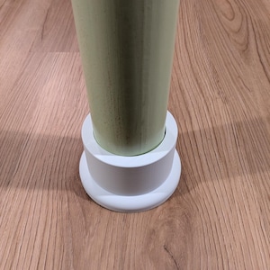 May include: A light green, cylindrical wooden post with a white base. The post is set on a wooden floor with a natural wood grain pattern. The base is a two-tiered design.