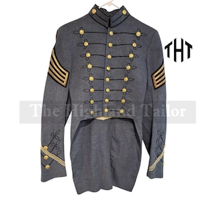 Puede incluir: Chaqueta gris de estilo militar con botones y adornos dorados. La chaqueta presenta ribetes negros, detalles dorados decorativos y rayas doradas en las mangas. El logotipo de The Highland Tailor es visible.