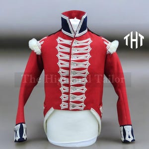 May include: A red military jacket with white detailing and silver buttons. The jacket features a navy blue collar and white epaulettes. The text "The Highland Tailor" is visible.