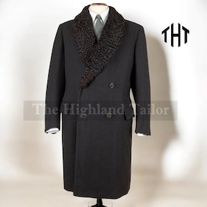 May include: A dark grey double-breasted overcoat featuring a textured, dark fur collar. The coat has two rows of buttons and side pockets. The text "The Highland Tailor" is visible. The coat is displayed on a mannequin.
