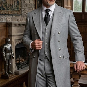 May include: A light grey, three-piece suit with a long coat. The suit features a waistcoat, trousers, and a double-breasted overcoat with silver buttons. The man wears a white shirt and a black tie. The text "THT The Highland Tailor" is visible.