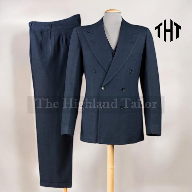 May include: A navy blue suit, including a double-breasted jacket and matching trousers, displayed on a mannequin. The jacket has black buttons and a notched lapel. The text "The Highland Tailor" is visible.