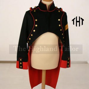Op de afbeelding: Zwarte jas in militaire stijl met rode accenten en gouden knopen. De jas heeft een hoge kraag en lange mouwen met rode manchetten. De achterkant heeft een lange, rode staart. De tekst "The Highland Tailor" is zichtbaar.