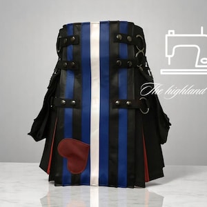 May include: A black, blue, and white striped kilt with a red heart-shaped patch. The kilt features black straps, silver rings, and a white vertical stripe down the center. The Highland Tailor logo is in the background.