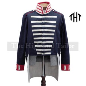 Puede incluir: Chaqueta militar azul marino con rayas horizontales blancas en el pecho y cuello alto con ribetes rojos y blancos. Los puños son rojos con detalles blancos. El texto "The Highland Tailor" es visible.