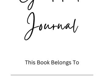 May include: A white journal with the words "Gratitude Journal" in elegant black script. Below, the text "This Book Belongs To" is printed, followed by three lines for personalization. The journal is designed for daily reflection.