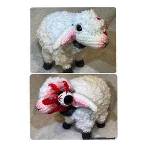 May include: A white crocheted plush sheep with a textured, fuzzy body, dark gray hooves, and pink inner ears. One side features a large, singular dark eye surrounded by red yarn detailing, while the other side shows a standard eye with a dark pupil.