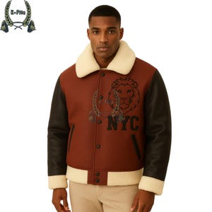 May include: A brown and black varsity jacket with a cream-colored shearling collar and trim. The jacket features a lion graphic and the letters "NYC" on the front. The sleeves are black, and the jacket has button closures.