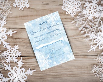 May include: A winter-themed invitation with a blue watercolor background and snowflake accents. The text reads "Winter Wonderland" and invites guests to celebrate the holiday season. Decorative paper snowflakes surround the invitation on a wooden surface.