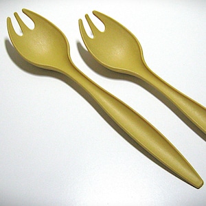 May include: Two yellow-green salad servers, each with a spoon-like bowl and three tines. The handles are long and slender. The servers are made of a matte material and are set against a white background.