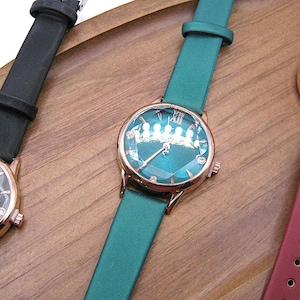 May include: Three elegant wristwatches with rose gold cases and leather straps in black, teal, and burgundy. Each watch features a unique dial design and the brand name "Tadi". The watches are displayed on a wooden surface.