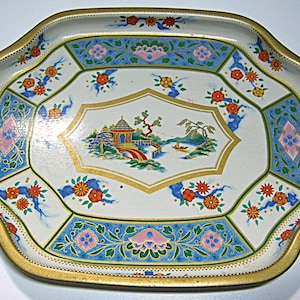 May include: Vintage metal serving tray with a decorative Asian-inspired design. The tray features a white background with a gold rim and a central landscape scene. The design includes blue, pink, and orange floral and geometric patterns.