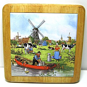 May include: Square wooden coaster with a ceramic tile featuring a Dutch countryside scene. The image shows windmills, cows, people in traditional clothing, and a red boat on a waterway. The coaster has a light brown wooden frame.