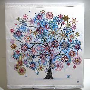 May include: A white canvas featuring a tree design adorned with colorful, sparkling snowflake ornaments. The tree trunk is black, and the snowflakes are in shades of blue, red, pink, and gold. The canvas is framed with a white border.