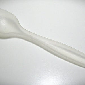May include: A translucent white plastic spork, a hybrid utensil combining a fork and spoon. The spork has three tines on one end and a spoon-like bowl. The handle is smooth and tapers to a point.