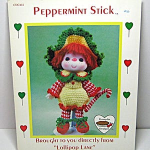 May include: A vintage Peppermint Stick doll pattern cover. The doll is crocheted with red, green, and yellow yarn. The doll has a red wig, a green and yellow hat, and a candy cane. The text reads "Peppermint Stick" and "Brought to you directly from Lollipop Lane."
