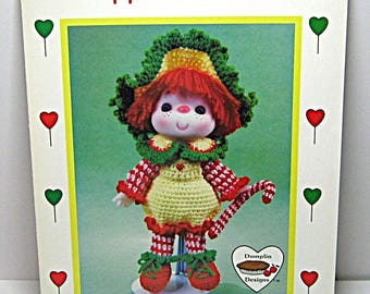 May include: A vintage Peppermint Stick doll pattern cover. The doll is crocheted with red, green, and yellow yarn. The doll has a red wig, a green and yellow hat, and a candy cane. The text reads "Peppermint Stick" and "Brought to you directly from Lollipop Lane."