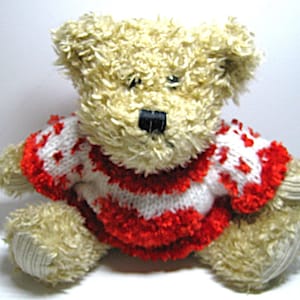May include: A plush teddy bear with light brown fur and a red and white sweater. The sweater has a striped pattern with red accents. The bear has a black nose and is sitting upright.