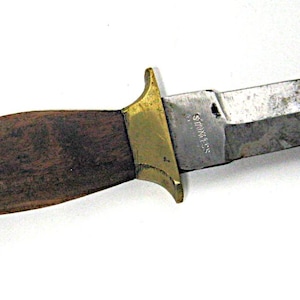 May include: A vintage dagger with a wooden handle and a stainless steel blade. The handle is dark brown with brass accents at both ends and a brass guard. The blade is silver and tapers to a sharp point.