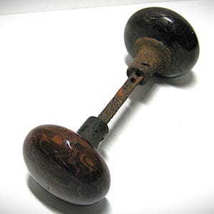 May include: A vintage door knob set featuring two smooth, dark brown, spherical knobs connected by a central metal spindle. The spindle and the collars connecting the knobs to the shaft show visible signs of oxidation and rust.