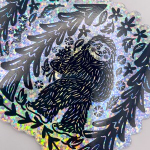 May include: A black and white illustration of a sloth holding flowers, surrounded by trees and flowers on a silver glitter background.