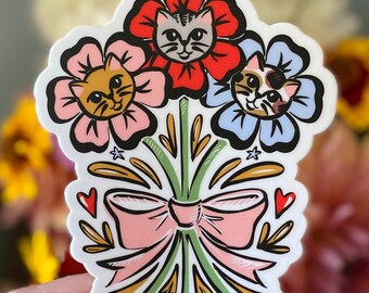 Può includere: Un adesivo con un bouquet di tre fiori con volti di gatto. Ogni fiore è di un colore diverso: rosso, rosa e blu. I fiori sono legati insieme da un fiocco rosa e hanno steli verdi. L'adesivo è firmato "Melissa Pottier".