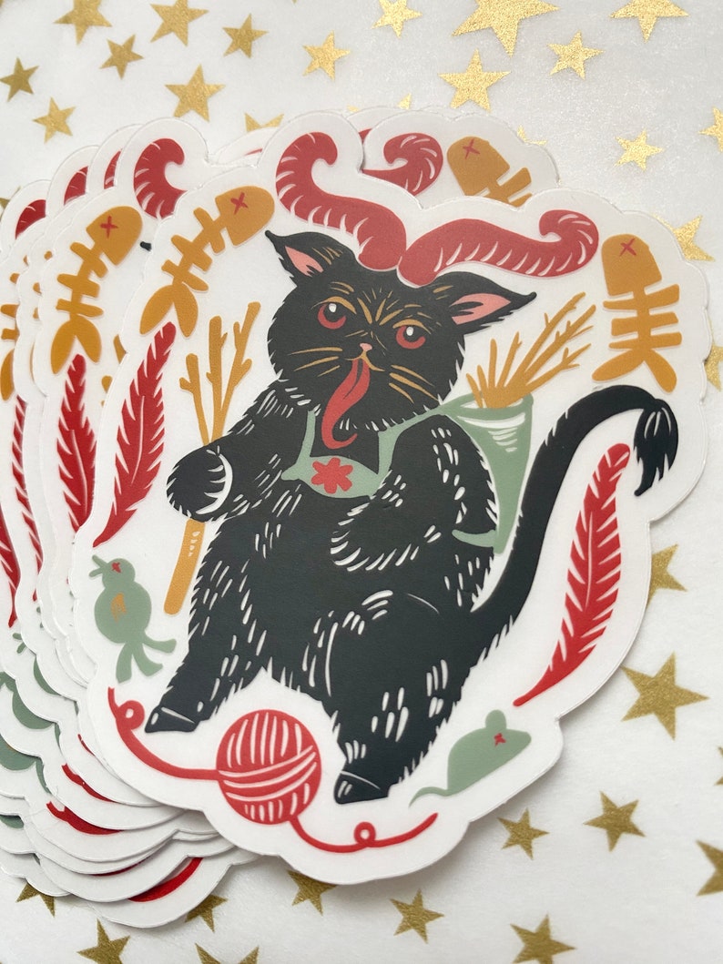 May include: A black cat with red horns and a red tongue is holding a bundle of sticks. The cat is surrounded by red, yellow, and green feathers, a red ball of yarn, and a green mouse. The cat is wearing a green vest with a red flower.