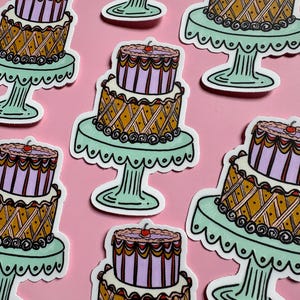 Pu&ograve; includere: Una collezione di adesivi con torte a due piani con disegni intricati. Le torte hanno una base marrone chiaro con un motivo a diamante, uno strato intermedio lavanda e una ciliegia in cima. Ogni torta poggia su un alzatina verde chiaro su sfondo rosa.