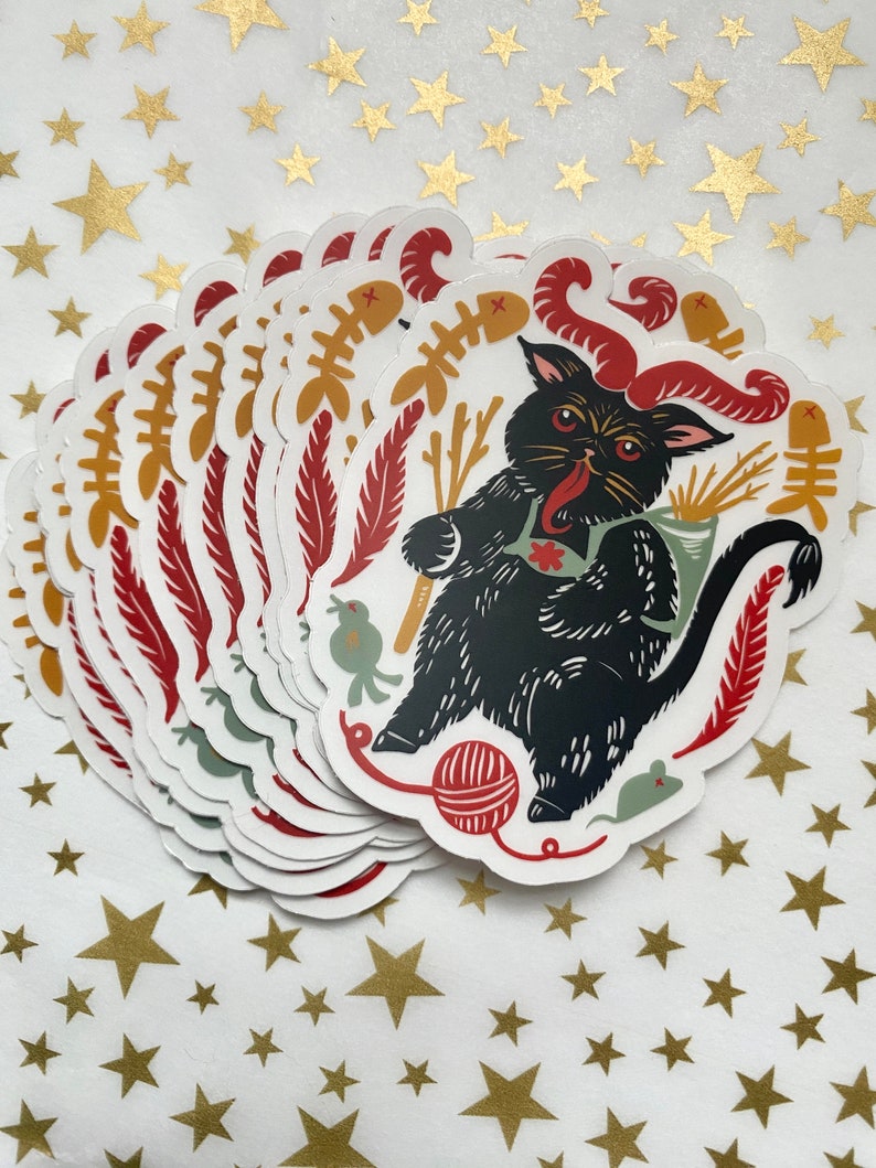May include: A stack of black cat stickers with red horns, a red bow tie, and a variety of other details. The cat is surrounded by a variety of objects, including a ball of yarn, a mouse, a bird, and a bone.