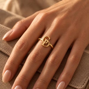 Handcrafted two initial ring in polished gold, 925 sterling silver, and rose gold. Features an elegant interlocking monogram with two custom initials for couples, lovers, or best friends. Dainty personalized letter band worn on woman's finger, displayed on stone tile and velvet ring box. Perfect romantic anniversary gift, promise ring, or birthday gift for her.
