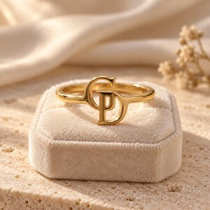 Handcrafted two initial ring in polished gold, 925 sterling silver, and rose gold. Features an elegant interlocking monogram with two custom initials for couples, lovers, or best friends. Dainty personalized letter band worn on woman's finger, displayed on stone tile and velvet ring box. Perfect romantic anniversary gift, promise ring, or birthday gift for her.