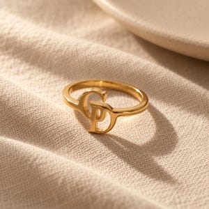 Handcrafted two initial ring in polished gold, 925 sterling silver, and rose gold. Features an elegant interlocking monogram with two custom initials for couples, lovers, or best friends. Dainty personalized letter band worn on woman's finger, displayed on stone tile and velvet ring box. Perfect romantic anniversary gift, promise ring, or birthday gift for her.