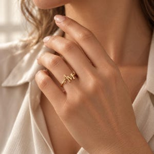Handcrafted two initial ring in polished gold, 925 sterling silver, and rose gold. Features an elegant interlocking monogram with two custom initials for couples, lovers, or best friends. Dainty personalized letter band worn on woman's finger, displayed on stone tile and velvet ring box. Perfect romantic anniversary gift, promise ring, or birthday gift for her.