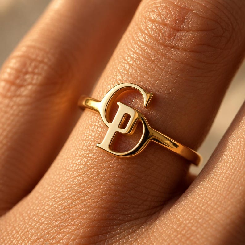 Handcrafted two initial ring in polished gold, 925 sterling silver, and rose gold. Features an elegant interlocking monogram with two custom initials for couples, lovers, or best friends. Dainty personalized letter band worn on woman's finger, displayed on stone tile and velvet ring box. Perfect romantic anniversary gift, promise ring, or birthday gift for her.