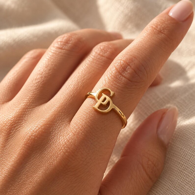Handcrafted two initial ring in polished gold, 925 sterling silver, and rose gold. Features an elegant interlocking monogram with two custom initials for couples, lovers, or best friends. Dainty personalized letter band worn on woman's finger, displayed on stone tile and velvet ring box. Perfect romantic anniversary gift, promise ring, or birthday gift for her.