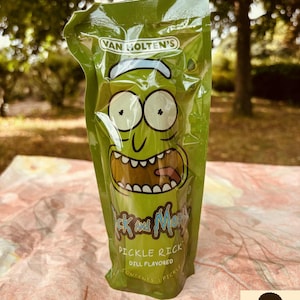 Pode incluir: Uma embalagem de plástico verde de picles com endro Pickle Rick da Van Holten. A embalagem apresenta uma imagem de desenho animado de Rick da série animada Rick and Morty. A embalagem está em uma superfície estampada.