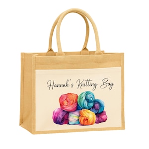 May include: A tan jute tote bag with a cream-colored front pocket. The pocket features the text "Hannah's Knitting Bag" above a watercolor image of colorful yarn balls. The bag has two handles for carrying.