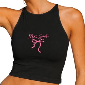 Op de afbeelding: Zwarte haltertop met de tekst "Mrs. Smith" in roze en een roze strik. De mouwloze top is nauwsluitend, ideaal voor warm weer of om te dragen als laagje.