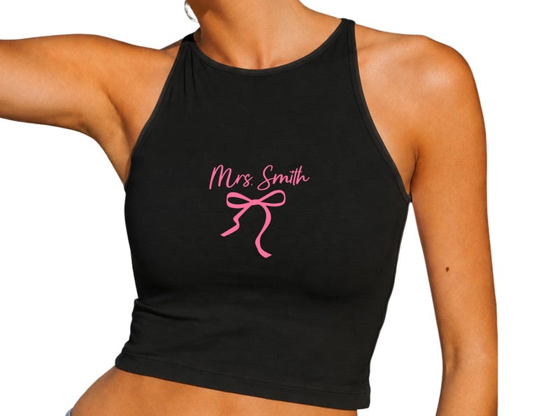 Op de afbeelding: Zwarte haltertop met de tekst "Mrs. Smith" in roze en een roze strik. De mouwloze top is nauwsluitend, ideaal voor warm weer of om te dragen als laagje.