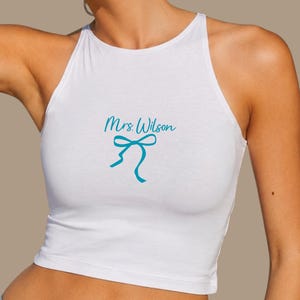 Op de afbeelding: Witte haltertop met de tekst "Mrs Wilson" in turquoise en een turquoise strik. De top is een crop top.