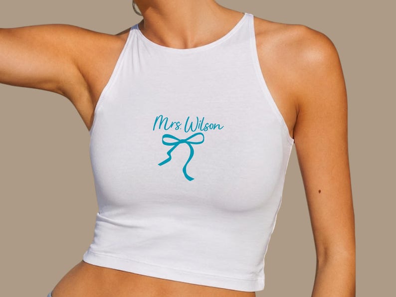 Op de afbeelding: Witte haltertop met de tekst "Mrs Wilson" in turquoise en een turquoise strik. De top is een crop top.