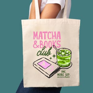 May include: Cream-colored tote bag with the text "Matcha & Books Club" in pink and green. The design includes a book, a matcha drink, and the text "One. More Sip. One more chapter."