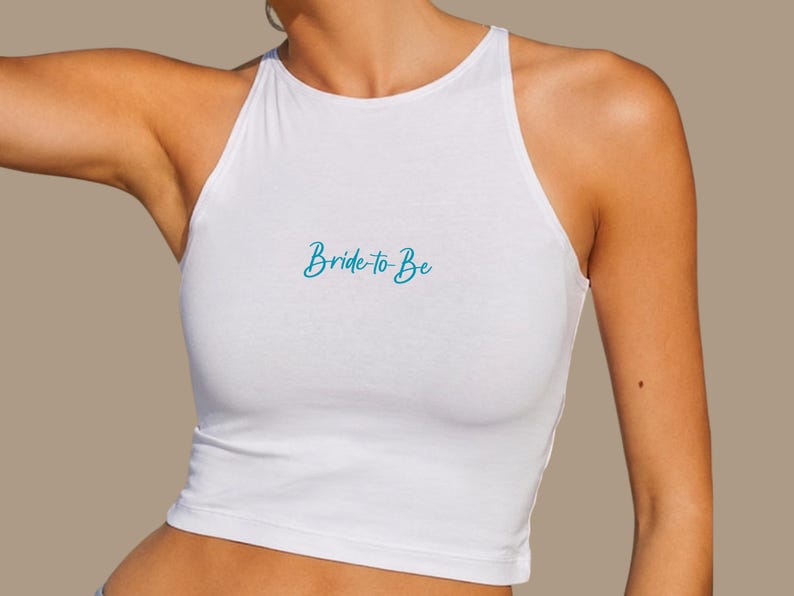 Op de afbeelding: Witte haltertop met de tekst "Bride to Be" in turquoise script. De top is mouwloos en gemaakt van een zacht, lichtgewicht materiaal. De tekst staat in het midden van de voorkant van de top.