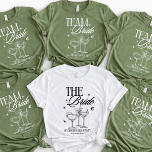 Puede incluir: Una colección de camisetas verdes oliva y blancas. Las camisetas verdes dicen "TEAM Bride" con un gráfico de cóctel y "MADISONS HEN PARTY PORTUGAL 2026". Una camiseta blanca dice "THE Bride" con un gráfico de cóctel.