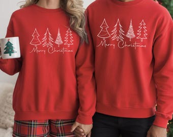May include: Two matching red crewneck sweatshirts featuring a white line art graphic of four distinct evergreen trees above the cursive text Merry Christmas. One sweatshirt is paired with red plaid shorts, and a white mug with a tree graphic.