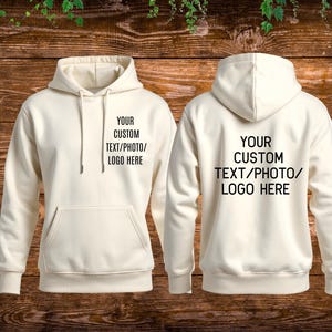 May include: A cream-coloured hooded sweatshirt shown from the front and back. The front features a kangaroo pocket and the black text "YOUR CUSTOM TEXT/PHOTO/LOGO HERE". The back displays the same black text centred on the upper portion.