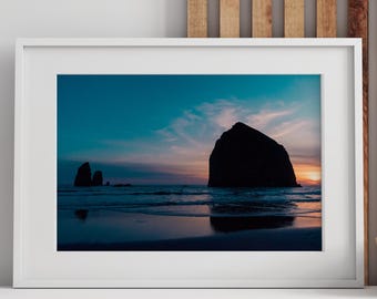 May include: A framed landscape photograph of a coastal scene. The image features a large rock formation silhouetted against a colorful sunset sky. The photograph is displayed on a wooden cabinet with decorative vases and a bowl.