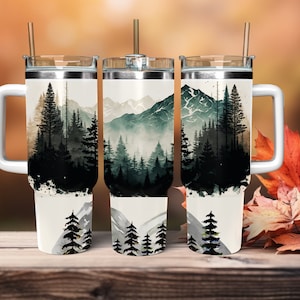 May include: White stainless steel tumbler with a black and green watercolor design of a mountain range and forest. The tumbler has a lid and a handle.