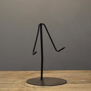 Könnte beinhalten: Ein schwarzer Metall-Präsentationsständer mit kreisförmiger Basis und gebogener Oberseite. Der Ständer hat ein minimalistisches Design, geeignet für die Präsentation verschiedener Artikel. Der Ständer ist aus Metall und hat eine matte Oberfläche.